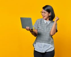 Ecstatic Asian woman with short hair celebrates success using a laptop.
