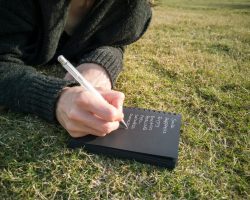 Person Writing on Book Lying Down on the Ground